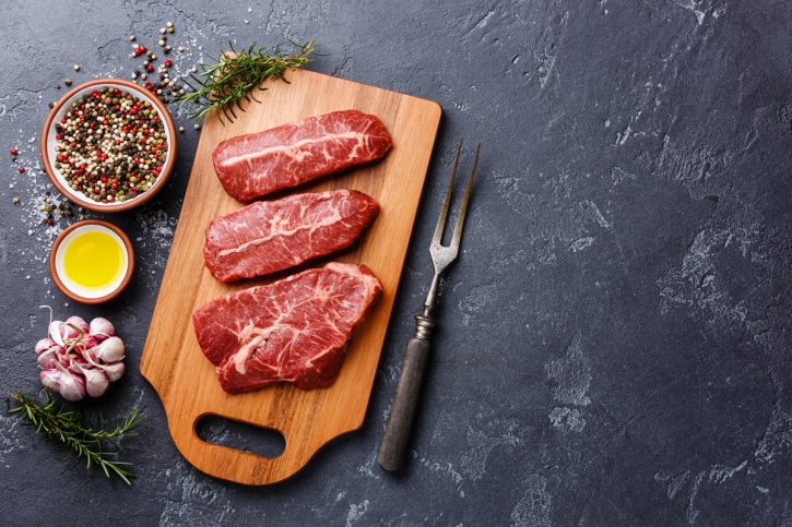Raw fresh meat Top Blade steaks on wood cutting board on dark ba